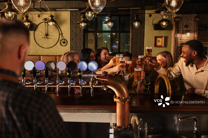 快乐的朋友们在酒吧柜台举杯畅饮啤酒图片素材