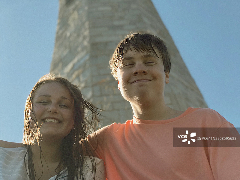 微笑的情侣在蓝天下靠近灯塔相拥图片素材