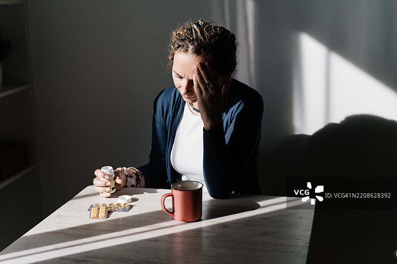 一位女性站在桌子旁，手中拿着黄色和绿色的药丸。图片素材