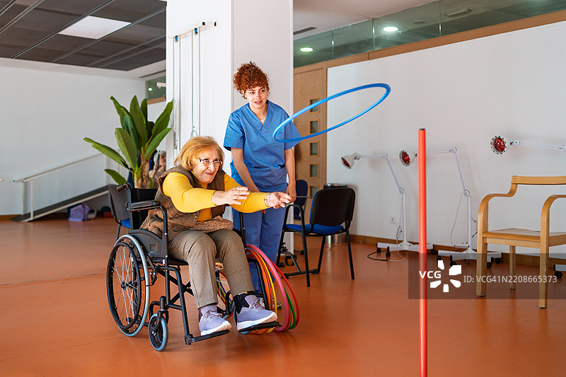 一位老年女性在康复中心的护士帮助下向目标投掷环圈图片素材