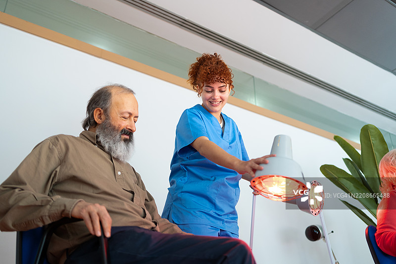 经验丰富的护士正在调整红外灯，为康复中心的老年患者治疗，支持医疗恢复过程图片素材