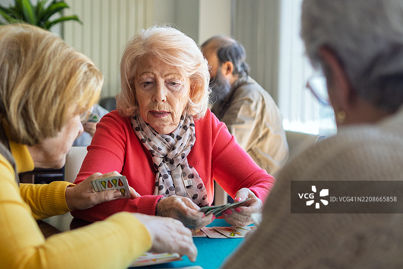 退休社区客厅中，年长女性们在聚会中玩牌，分享友谊与微笑。图片素材