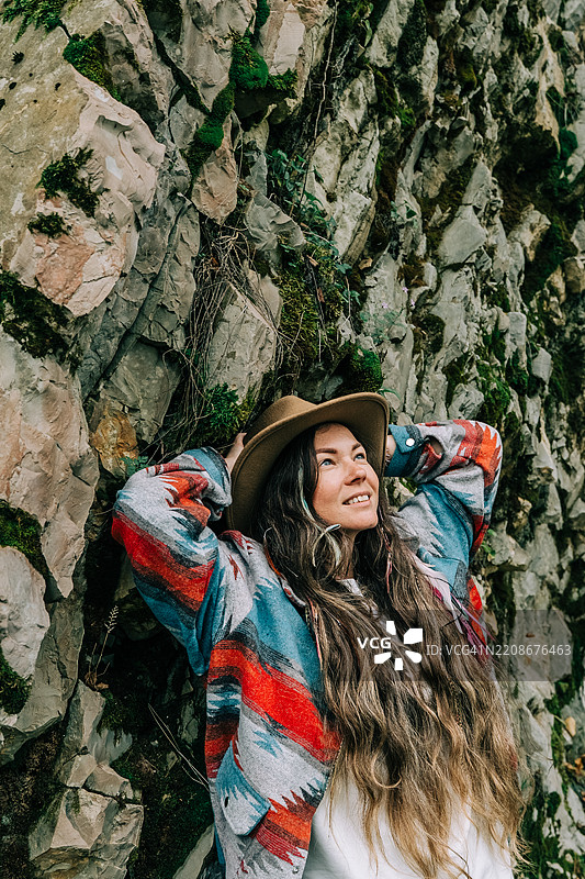 戴着牛仔帽的女人靠在苔藓覆盖的岩石上图片素材