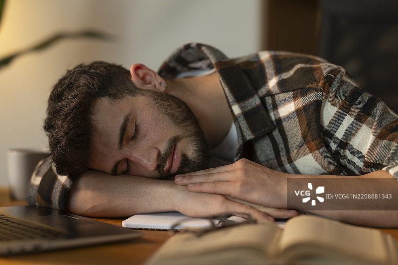 年轻男子在长时间学习后趴在桌子上睡觉图片素材