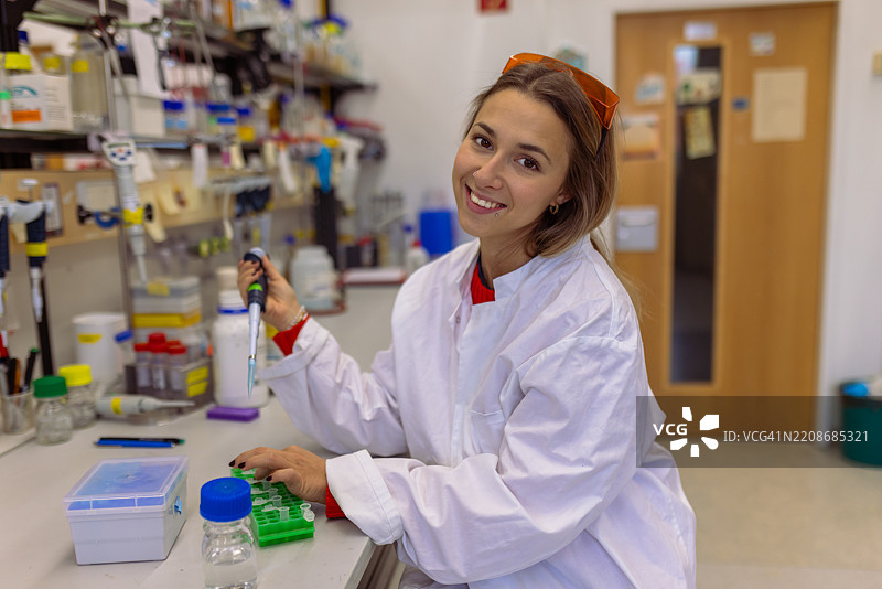 微笑的女性科学家在进行PCR测试时使用移液器的肖像图片素材