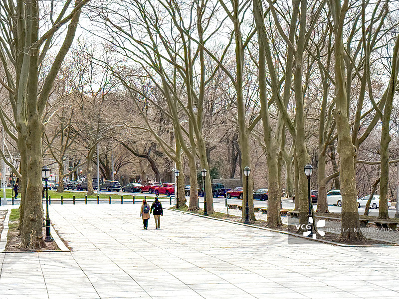 两个人在纽约市的广场上手牵手走在树木旁边图片素材