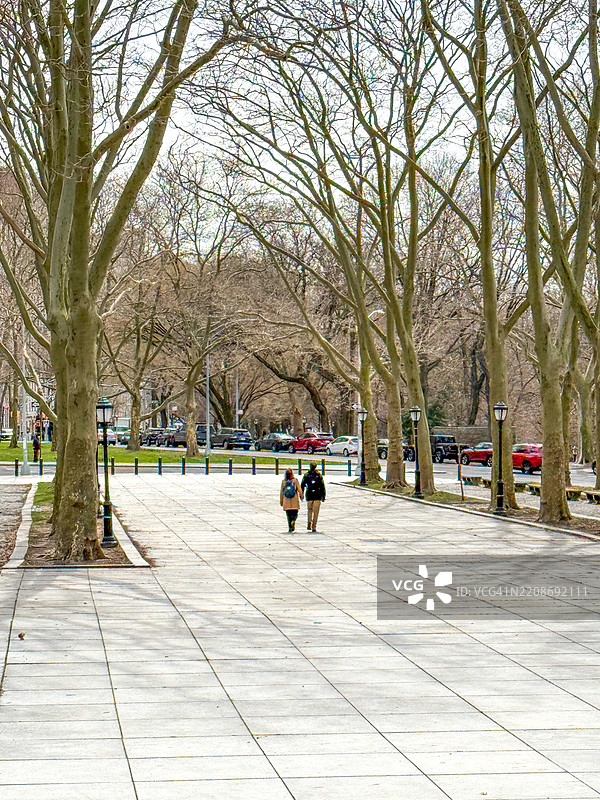 两个人在纽约市的广场上手牵手走在树木旁边图片素材