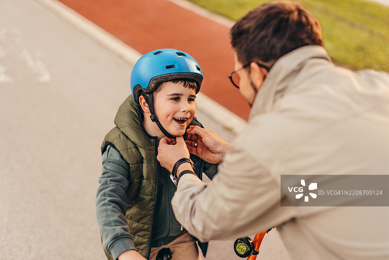 关心的父亲在骑行前为儿子系好自行车头盔图片素材