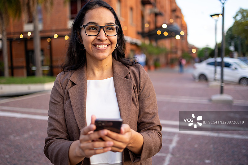 微笑的职业女性在户外城市环境中使用智能手机图片素材