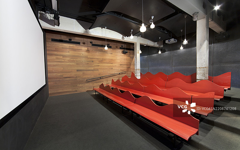 在罗西·里维特访客中心（国家公园管理局）的电影院内，涂漆的木制长椅座位。电影院由混凝土柱和梁、投影屏幕、铁丝网墙、木质墙板和电气照明构成。图片素材