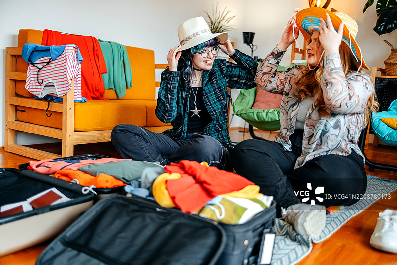 少女们在家中一起打包行李箱，准备度假，并试戴帽子。图片素材