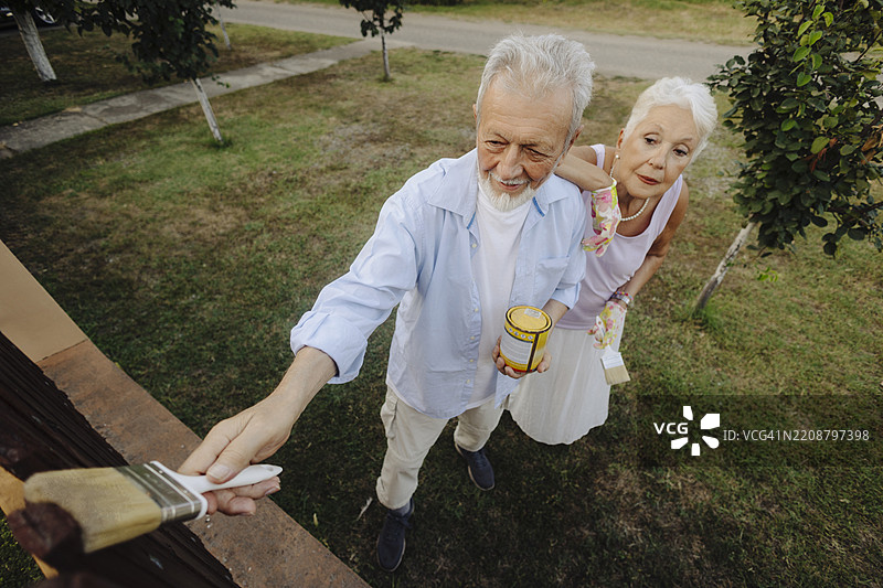 一对老年夫妇正在家里粉刷围栏。图片素材
