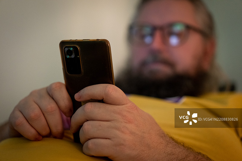 疲惫的斯堪的纳维亚男子在夜晚看着智能手机，留着胡子。图片素材