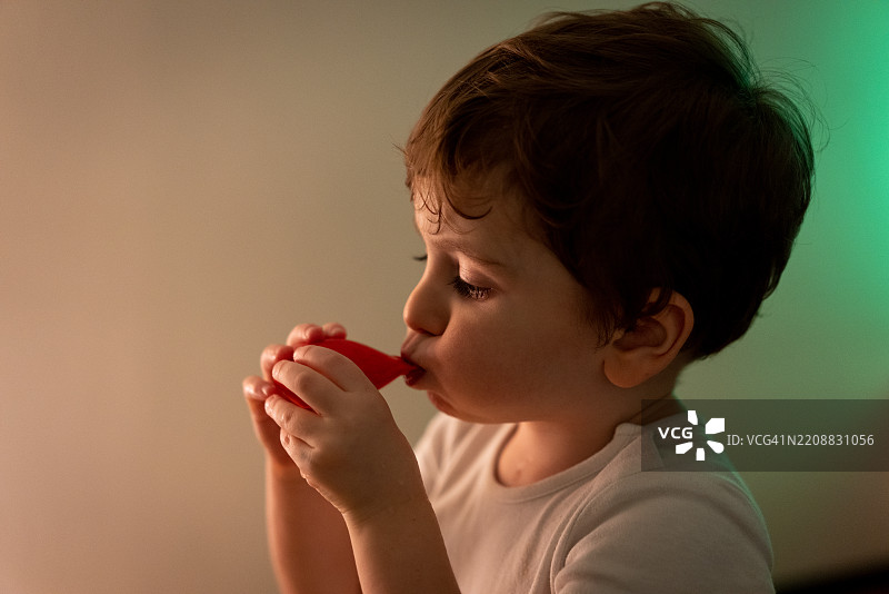 小男孩独自坐在白墙旁，嘴里吹着气球。图片素材