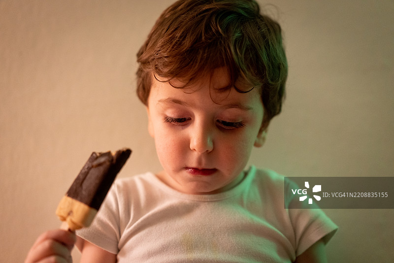 可爱的小男婴穿着尿布，坐在白墙前的地板上独自吃冰淇淋。图片素材