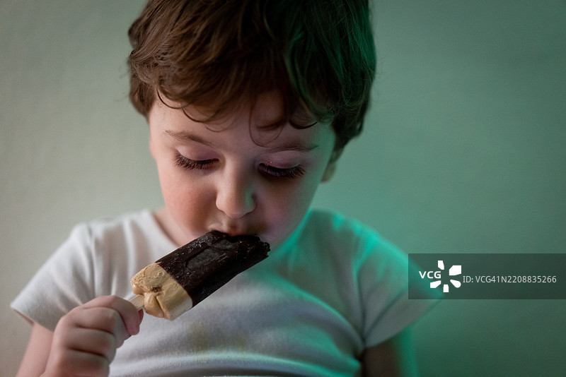 可爱的小男孩穿着尿布，独自坐在白墙前的地板上吃冰淇淋。图片素材