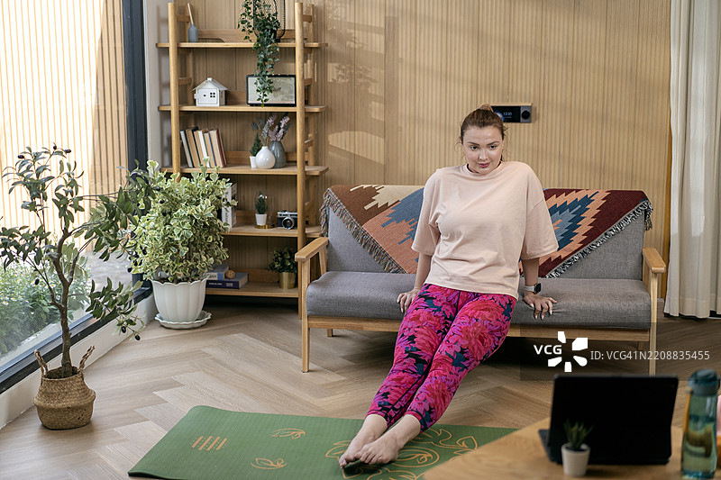 年轻女性在家中观看健身视频，进行热身运动。图片素材