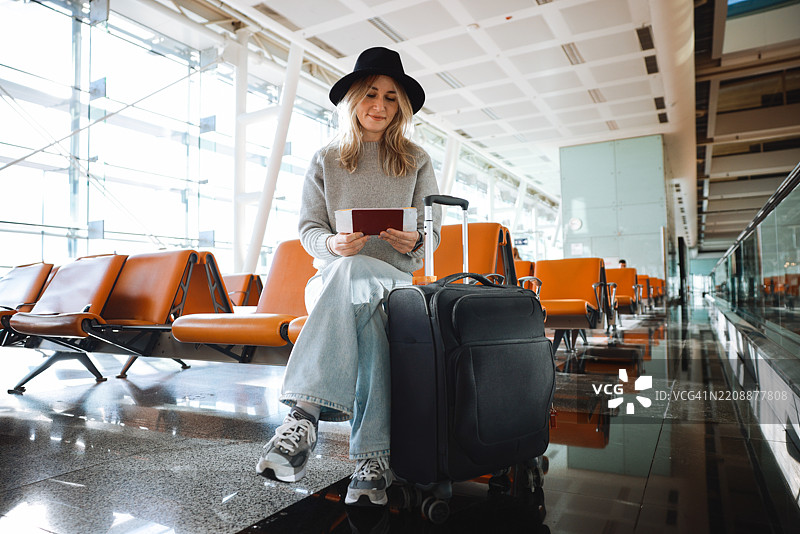 微笑的女性坐在机场椅子上手持护照图片素材