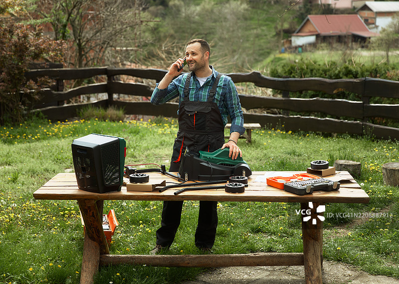 一位英俊的中年男子正在组装割草机并打电话。图片素材