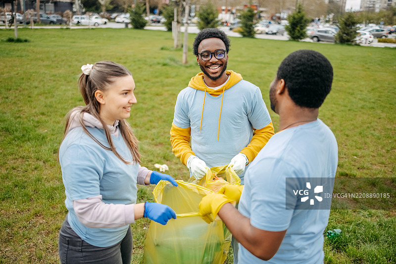 一群年轻人在公园里一起快乐地进行社区服务，收集垃圾。图片素材