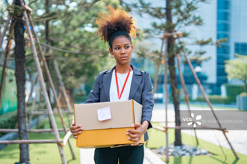 一位失业的女性提着纸箱离开办公室，因大萧条裁员。图片素材