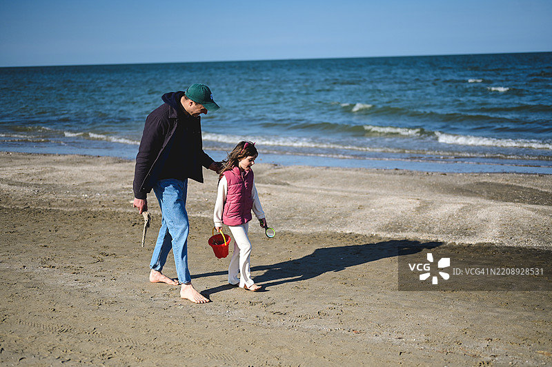 父亲和女儿在阳光明媚的日子里漫步在海滩上图片素材