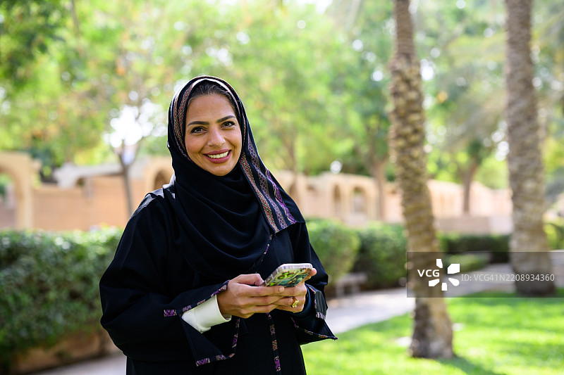微笑的穆斯林女性在户外手持智能手机的肖像图片素材
