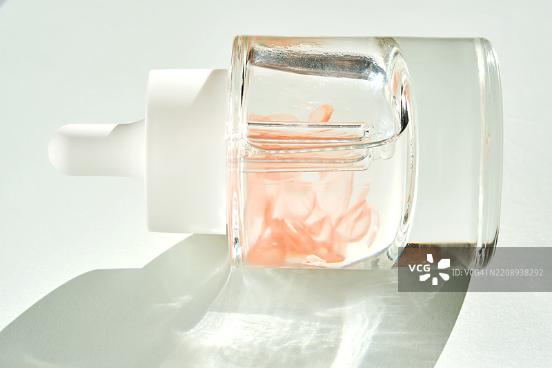 一瓶美丽的精华液，阳光下洒满花瓣。图片素材