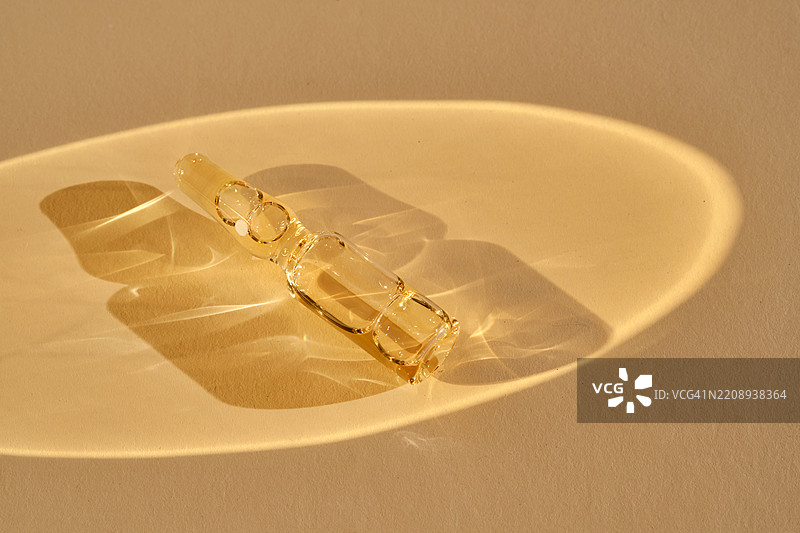 一个装有化妆品或医疗产品的安瓿瓶，背景为米色，散发着美丽的金色光芒。图片素材