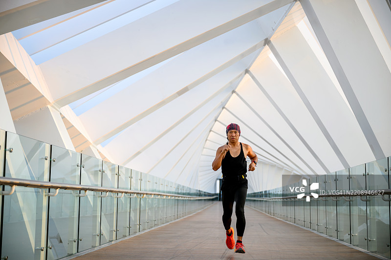 全身镜头拍摄一名跑者在现代人行天桥上训练，天桥具有几何建筑特征。图片素材