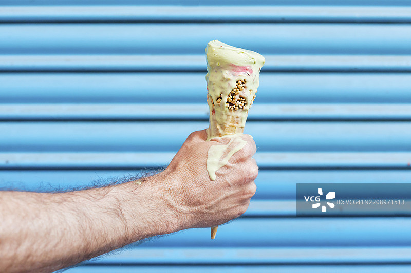 男人手持在蓝色背景下融化的冰淇淋蛋筒图片素材