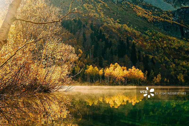 秋天的树叶在日出时映照在山湖的水面上图片素材