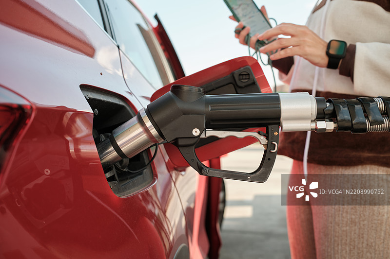 女性在加油站为汽车加油，手持智能手机 - 经济与燃料危机概念图片素材