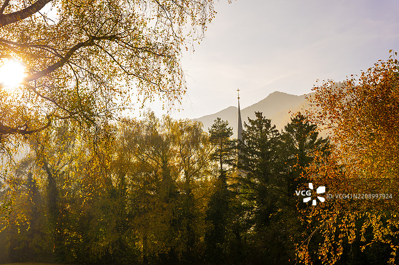 美丽的秋季森林、教堂塔楼、山脉和阳光明媚的天空，阳光洒在巴德拉加兹的晴朗日子里图片素材