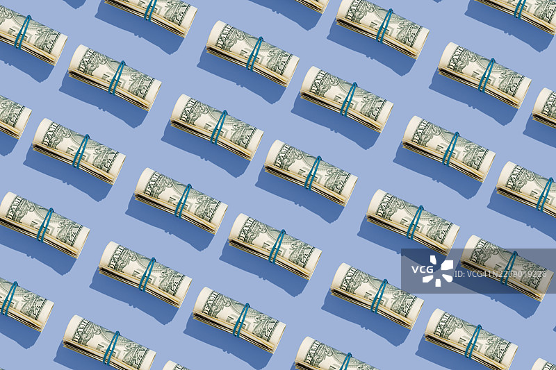 在蓝色背景上重复摆放的美金钞票卷图片素材