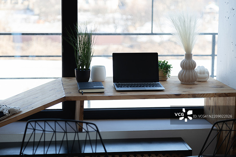 窗边的木桌上放着一台笔记本电脑和一本笔记本的工作场所。图片素材