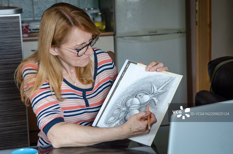 一位年长女性在视频通话会议中展示她的铅笔画，参加在线课程。图片素材