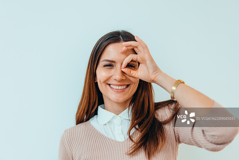 微笑的女性在简约的浅色背景下用手指调皮地做手势图片素材