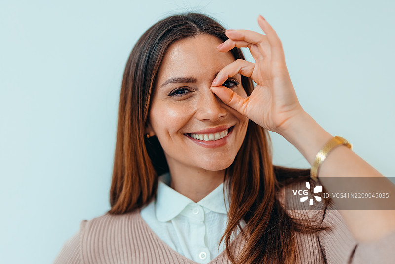 微笑的女性用手在左眼上方做圆形手势图片素材
