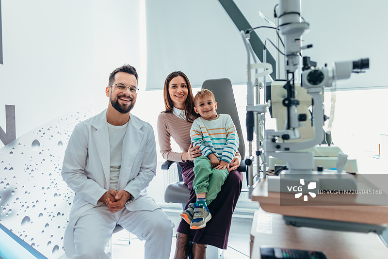 快乐的家庭在验光师诊所与孩子和验光设备一起图片素材