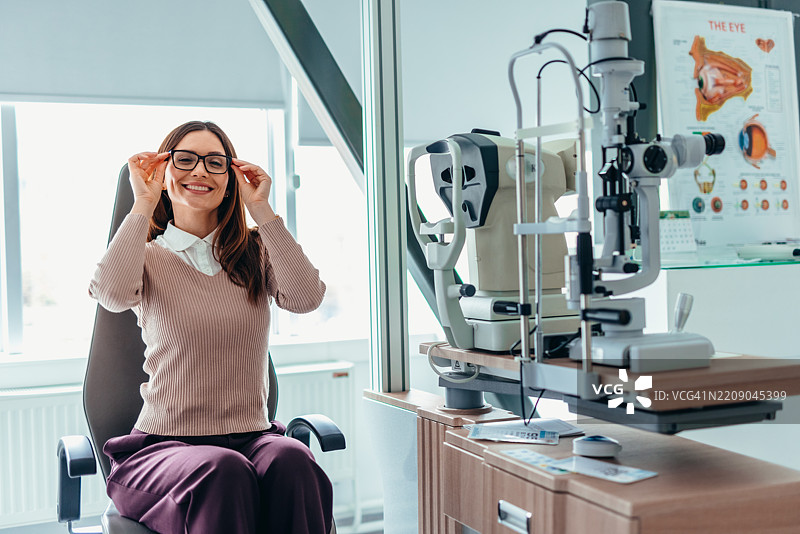 在验光师诊所微笑的女性正在调整眼镜，靠近眼科检查台。图片素材