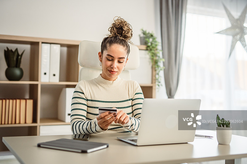 一位年轻女性在办公室工作时手持卡片在线购物图片素材