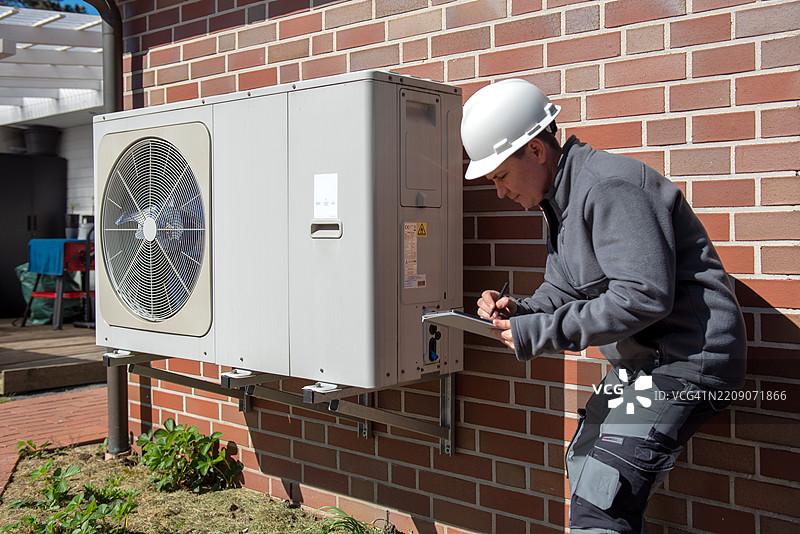 技术人员在白天检查安装在砖墙上的空调设备。图片素材
