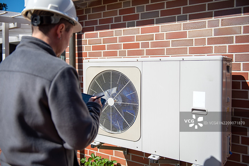 技术人员在户外用智能手机检查砖墙上的暖通空调设备。图片素材