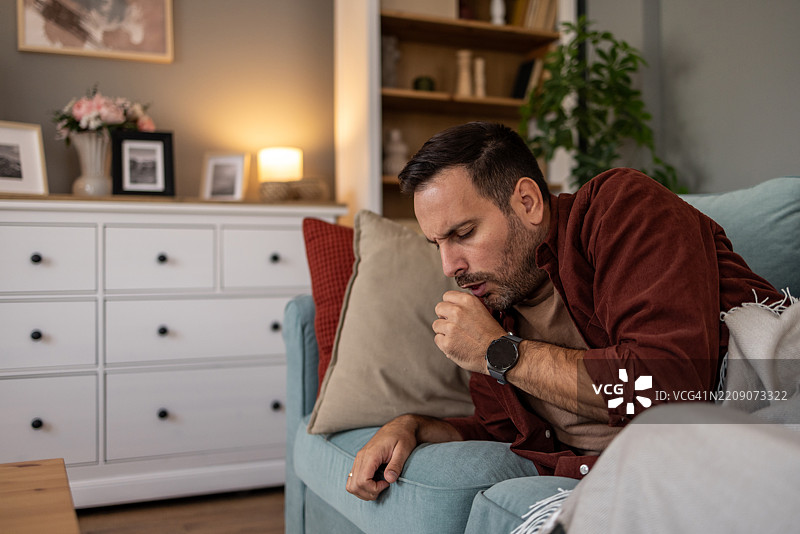 生病的男人在家里的沙发上咳嗽图片素材