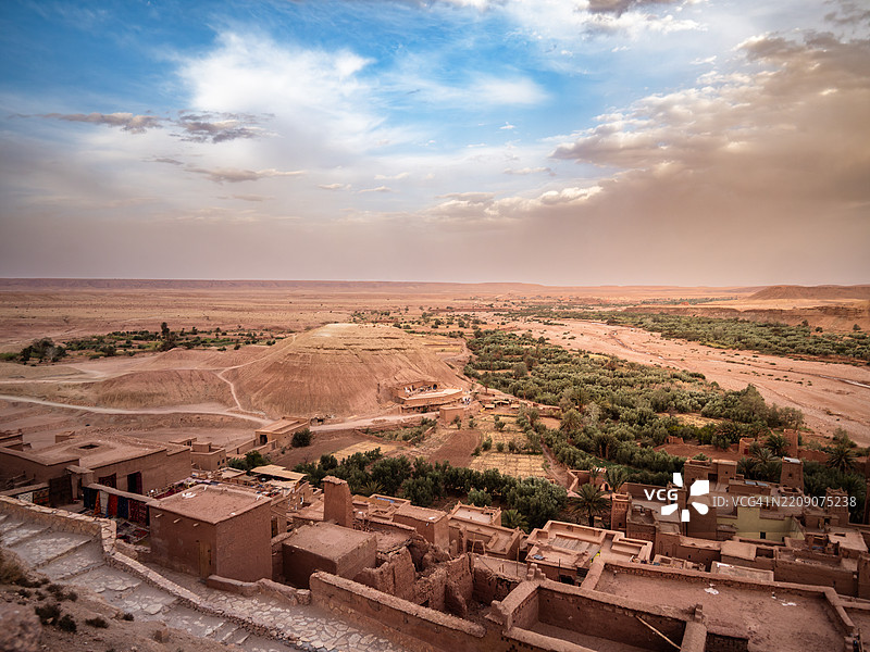 高处俯瞰著名的贝尔贝尔人防御村艾特·本哈杜(Aït Benhaddou Kasbah)及其周围的乌尼拉谷,夕阳下的古老夯土房屋、干涸的河床、绿洲和山丘,联合国教科文组织世界遗产 - 瓦尔扎扎特 - 摩洛哥。图片素材
