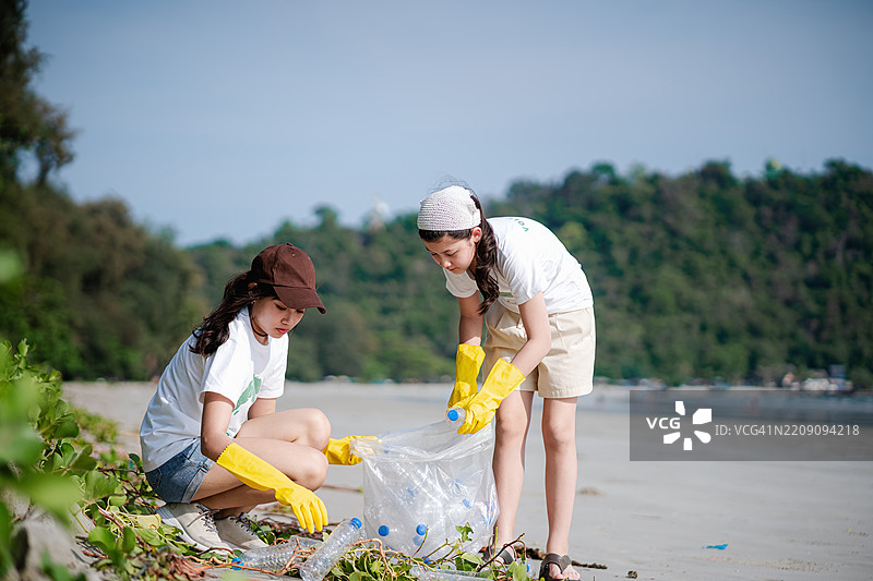 两个姐妹在夏季周末志愿服务，收集垃圾袋中的垃圾，参与减少海洋污染的活动。图片素材