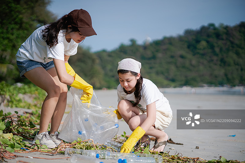 两个姐妹在夏季周末作为志愿者，收集垃圾并装入垃圾袋，参与减少海洋污染的活动。图片素材