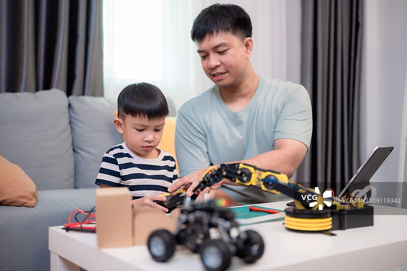 父亲和儿子在阳光明媚的客厅里进行机器人和编程的STEM项目。图片素材