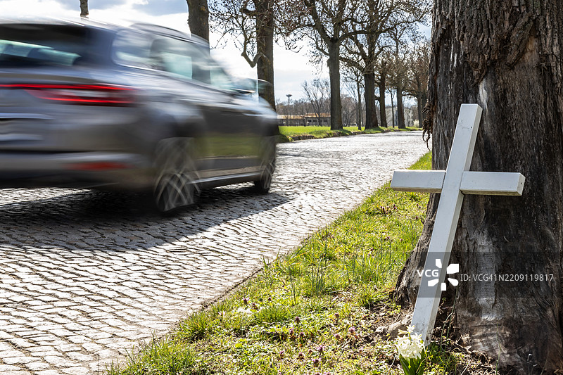 一辆快速行驶的汽车经过一棵树，树上挂着一座纪念十字架，那里曾发生过可怕的交通事故。图片素材